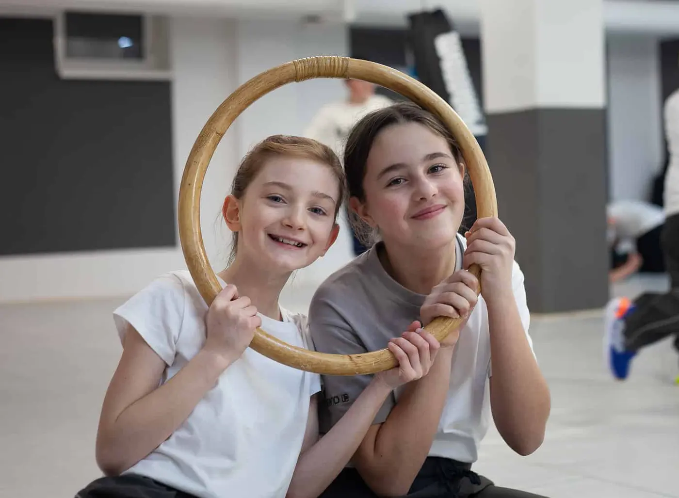 Zwei Mädchen lachen beim Kindertraining durch einen Holzring